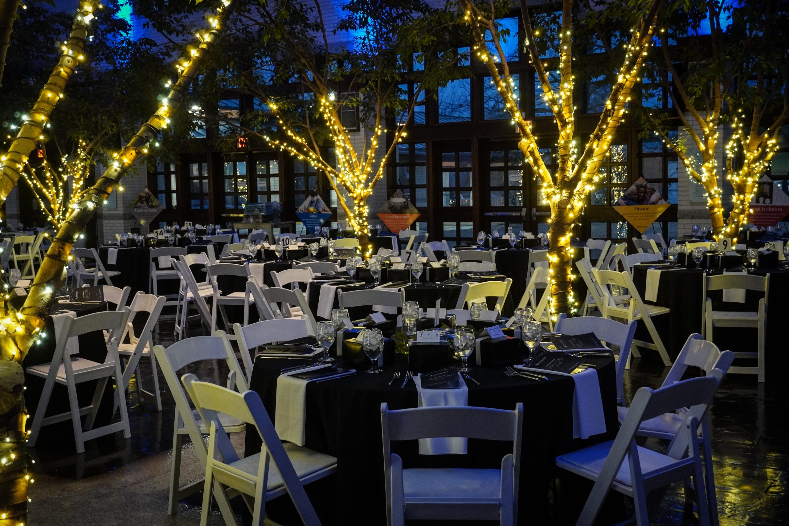 venue atrium decorated for gala with glowing trees, white chairs and black table cloths