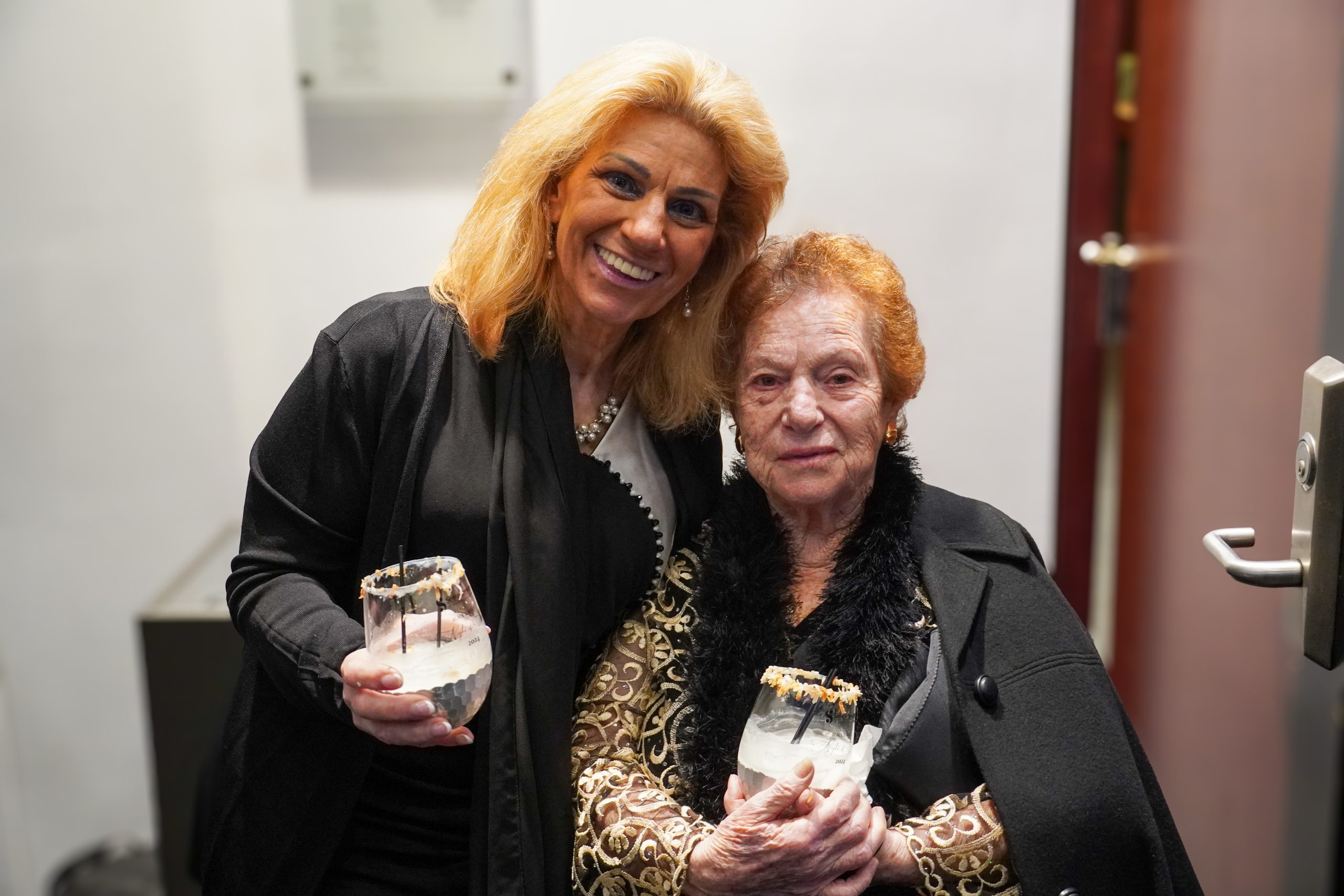 two caucasian females smiling at camera holding glasses