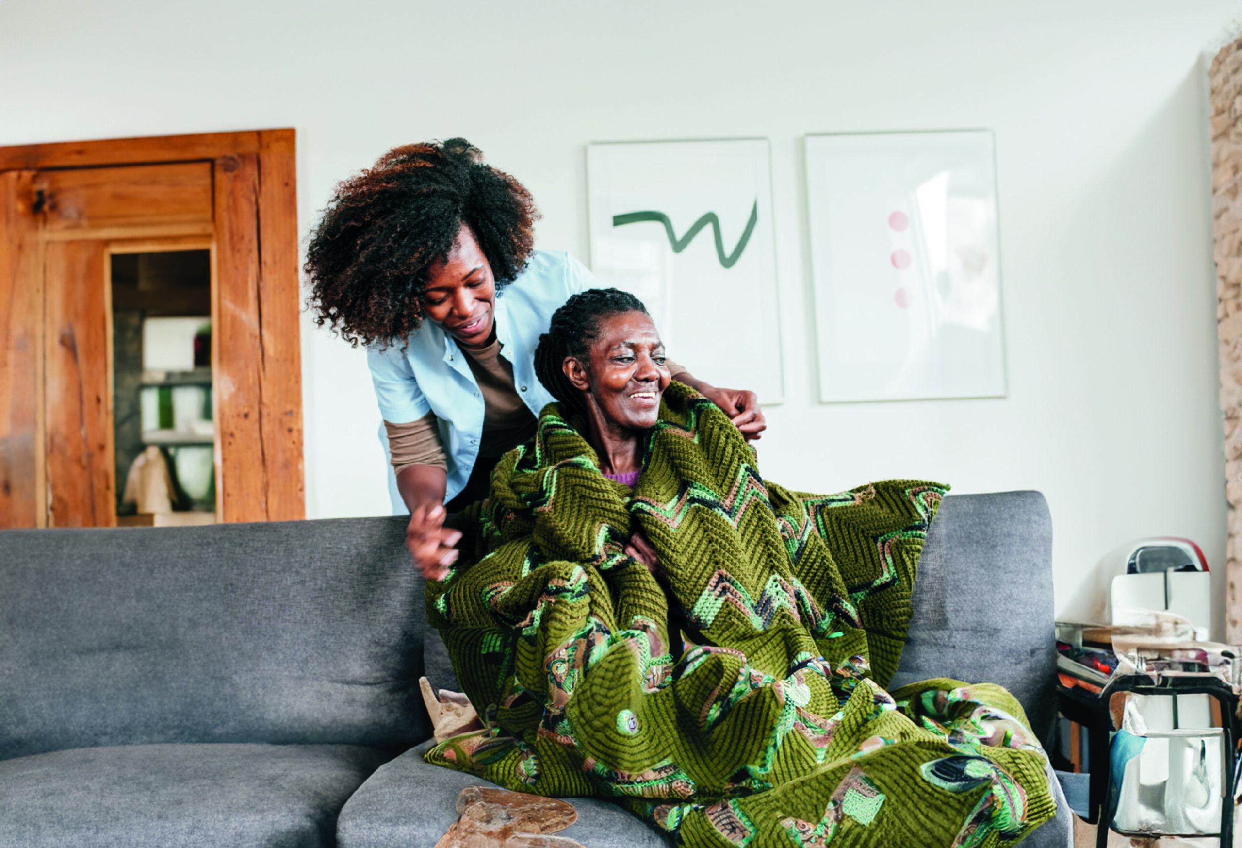 Young African American woman placing blanket on older African American woman.