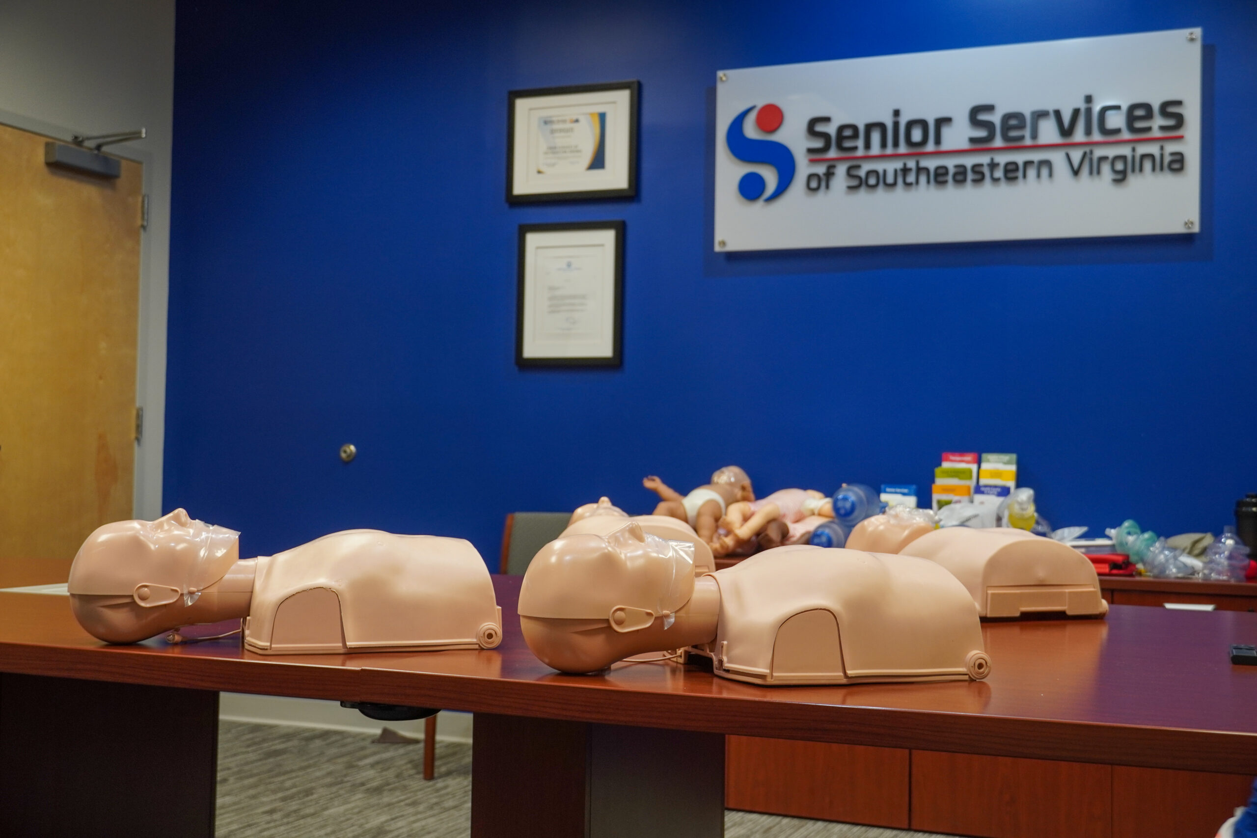 CPR dummies laying on table with Senior Services Logo in background