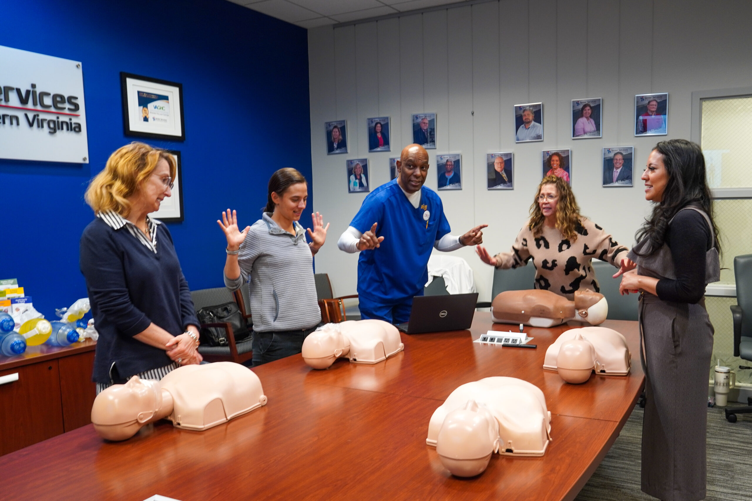 Five adults surrounding table with CPR dummies