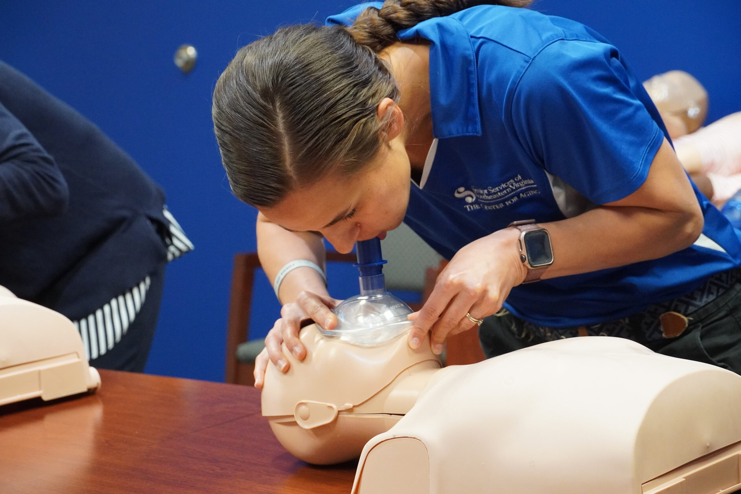 White female with blue shirt giving CPR dummy mouth to mouth