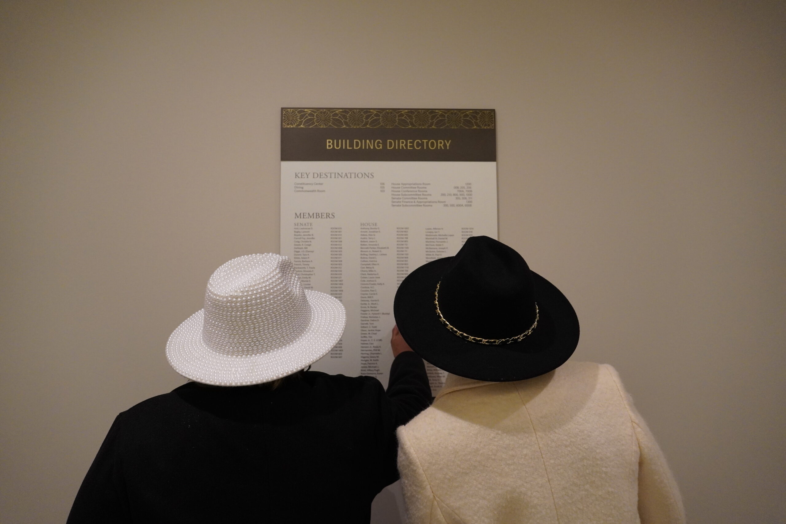 two women in hats looking at a sign