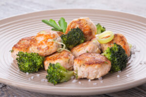 Plate of salmon meatballs with vegetables on a wooden table