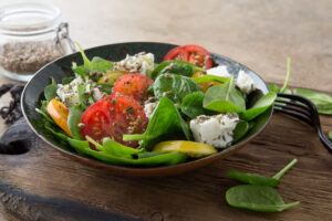 a plate of salad with tomatoes, spinach and feta cheese on the table