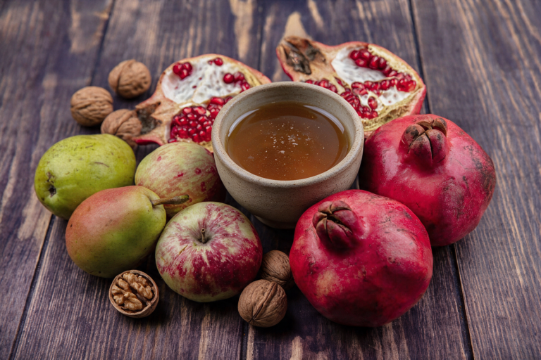 photo of pomegranates apples and pears surrounding a bowl of honey