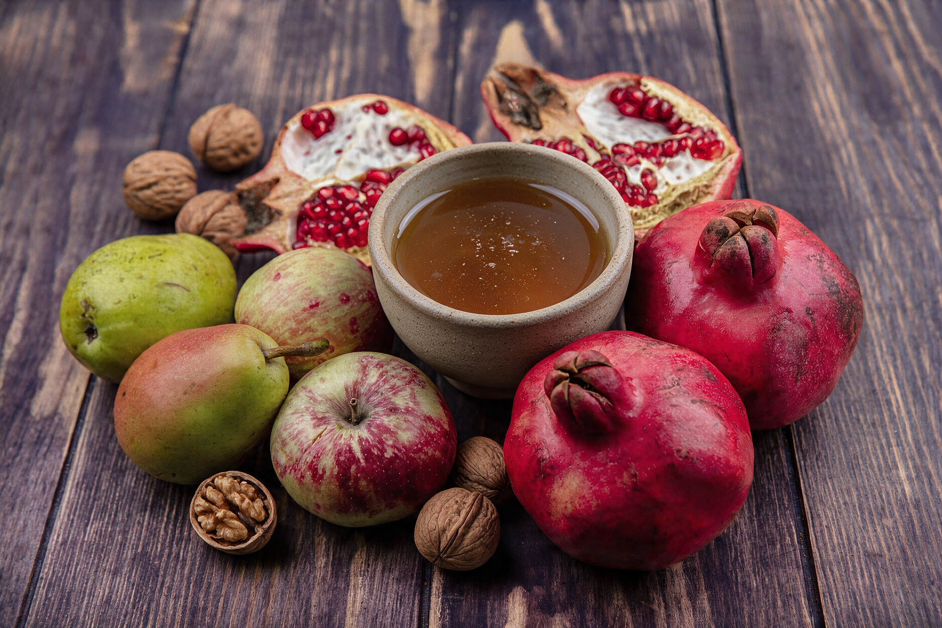 photo of pomegranates apples and pears surrounding a bowl of honey